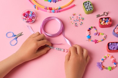 Child making beaded jewelry and different supplies on pink background, above view. Handmade accessories