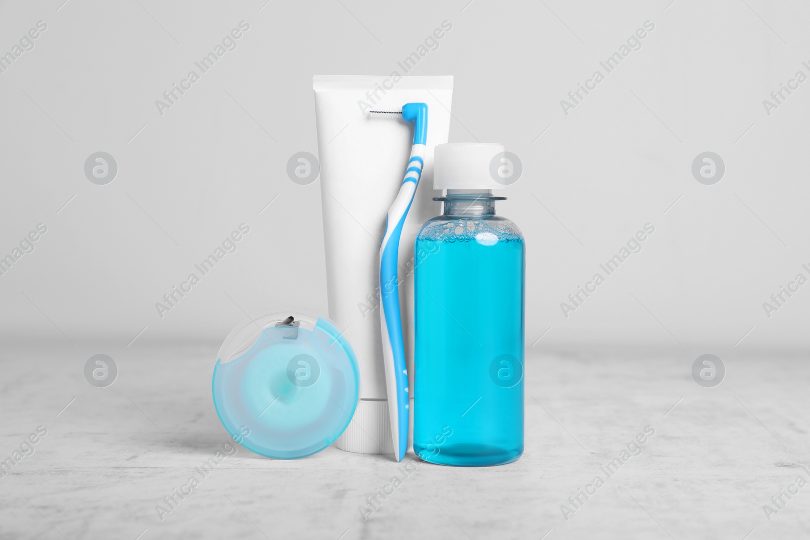 Photo of Dental floss and different teeth care products on light grey textured table