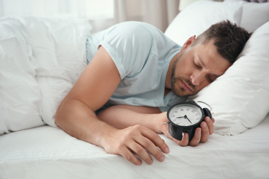 Man sleeping with alarm clock at home in morning