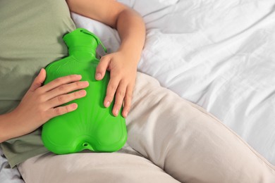 Young woman using hot water bottle to relieve cystitis pain on bed, closeup