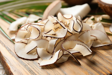 Photo of Pile of tasty coconut chips on wooden board, closeup