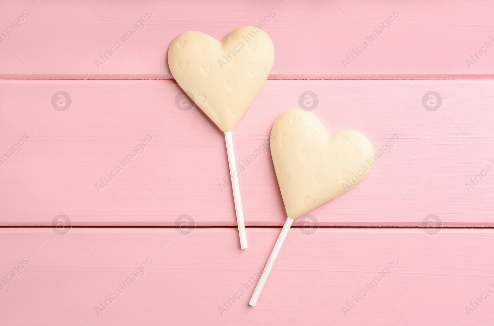 Photo of Chocolate heart shaped lollipops on pink wooden table, flat lay