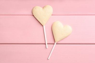 Chocolate heart shaped lollipops on pink wooden table, flat lay