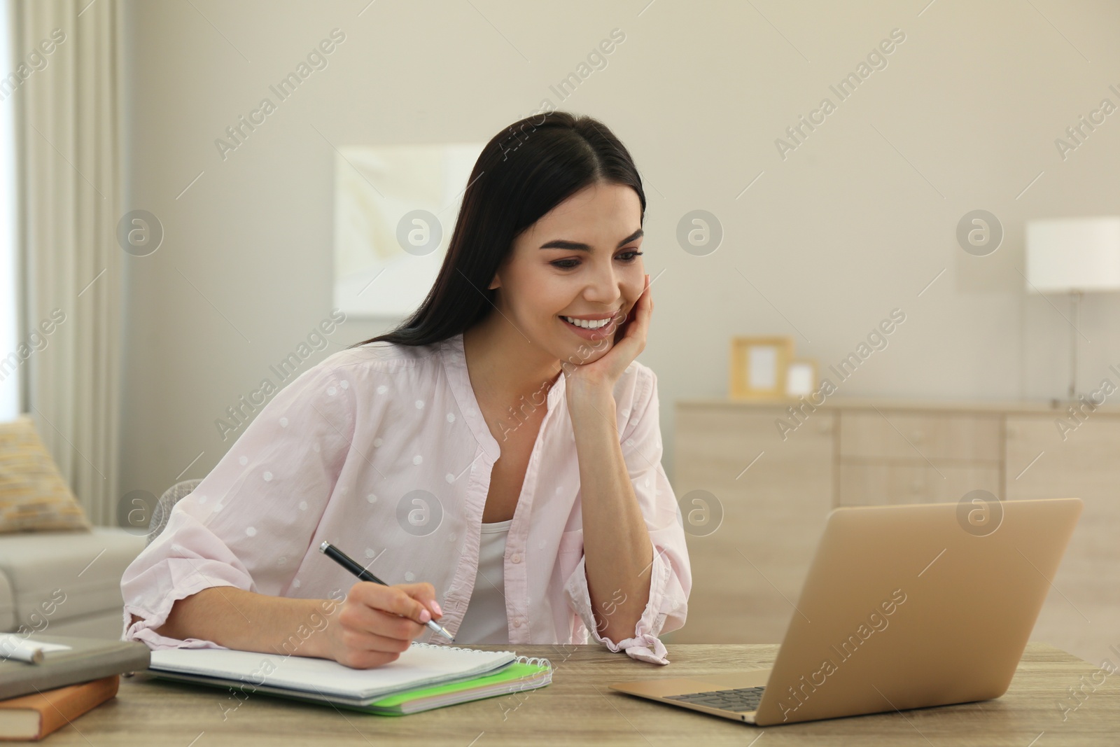 Photo of Young woman taking notes during online webinar at table indoors