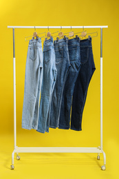 Rack with different jeans on yellow background