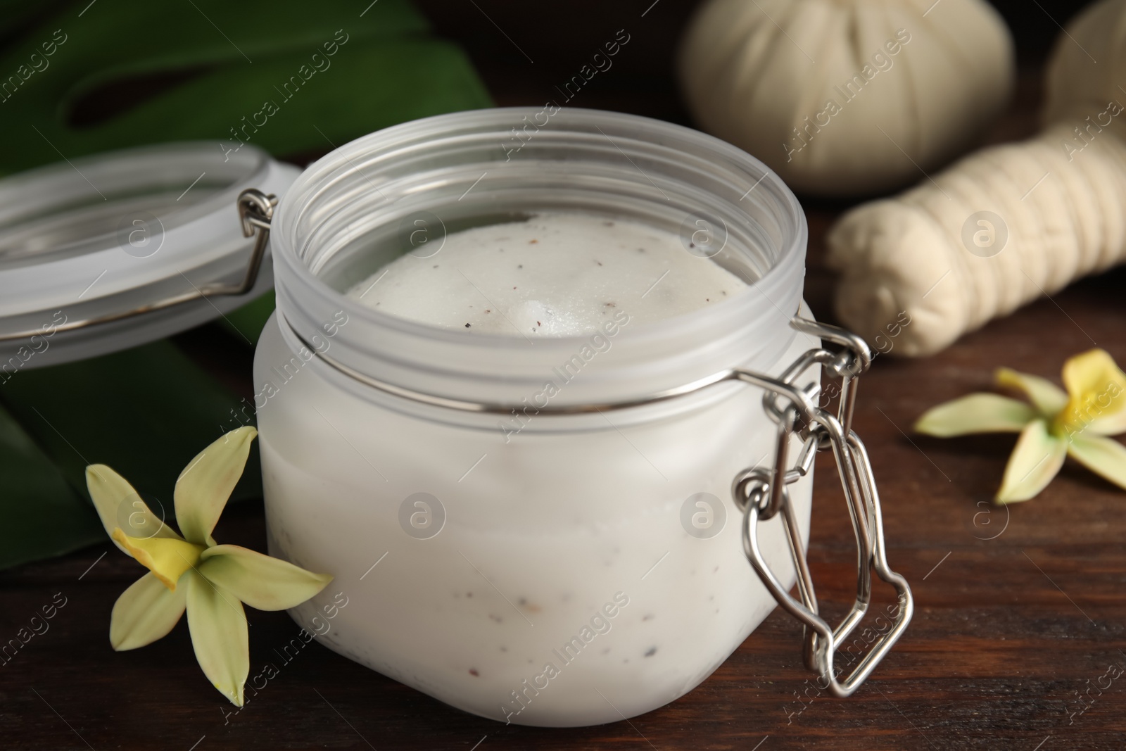 Photo of Jar of salt scrub and orchid flower on wooden table, closeup