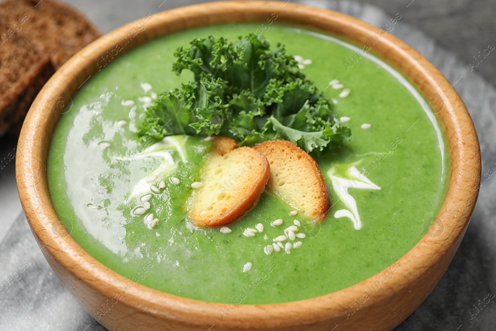 Photo of Tasty kale soup with croutons on grey marble table, closeup