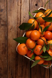 Fresh tangerines with green leaves in crate on wooden table, top view