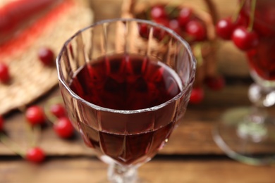 Delicious cherry wine in glass on wooden table, closeup