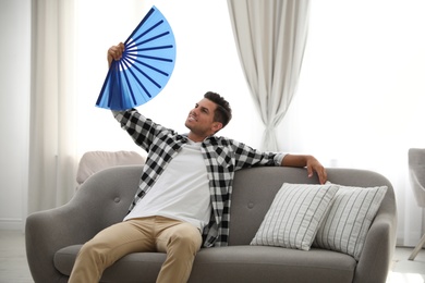 Photo of Man with hand fan sitting on sofa. Summer season