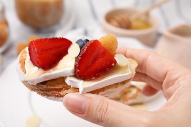 Photo of Woman holding sandwich with brie cheese, fresh berries, honey and almond flakes at table, closeup