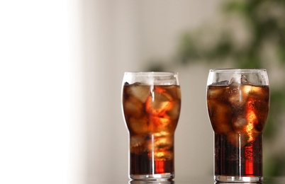 Photo of Glasses of cola with ice on table against blurred background. Space for text