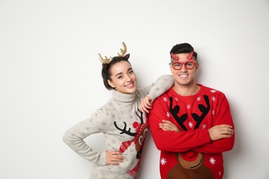 Photo of Couple in Christmas sweaters, deer headband and party glasses on white background