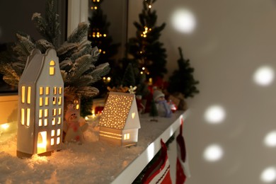 Photo of Christmas atmosphere. Beautiful glowing houses, fir trees, artificial snow and toys on window sill indoors. Space for text