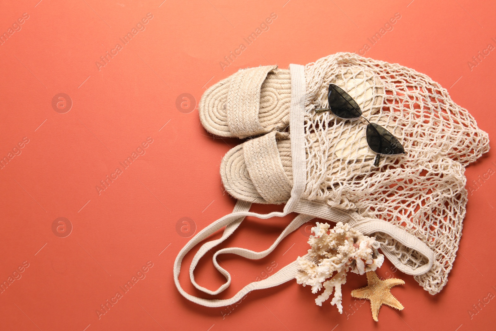 Photo of String bag, sunglasses, slippers, starfish and coral on color background, top view. Space for text