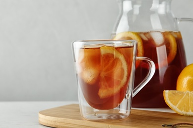 Cup and jug of refreshing iced tea on white table against light background. Space for text