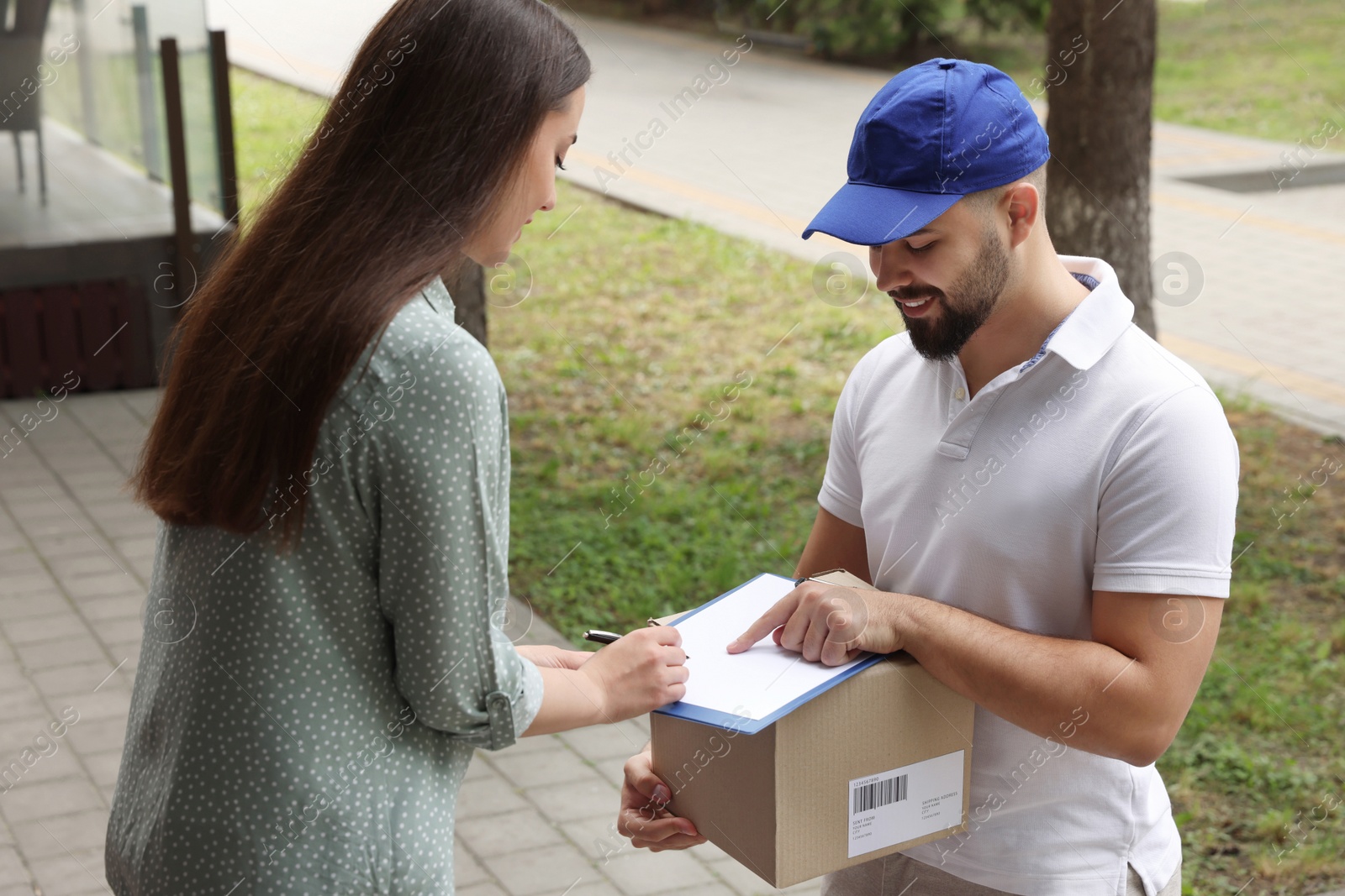 Photo of Woman signing for delivered parcel outdoors. Courier service