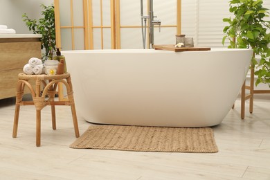 Stylish bathroom interior with ceramic tub, spa products and green houseplants