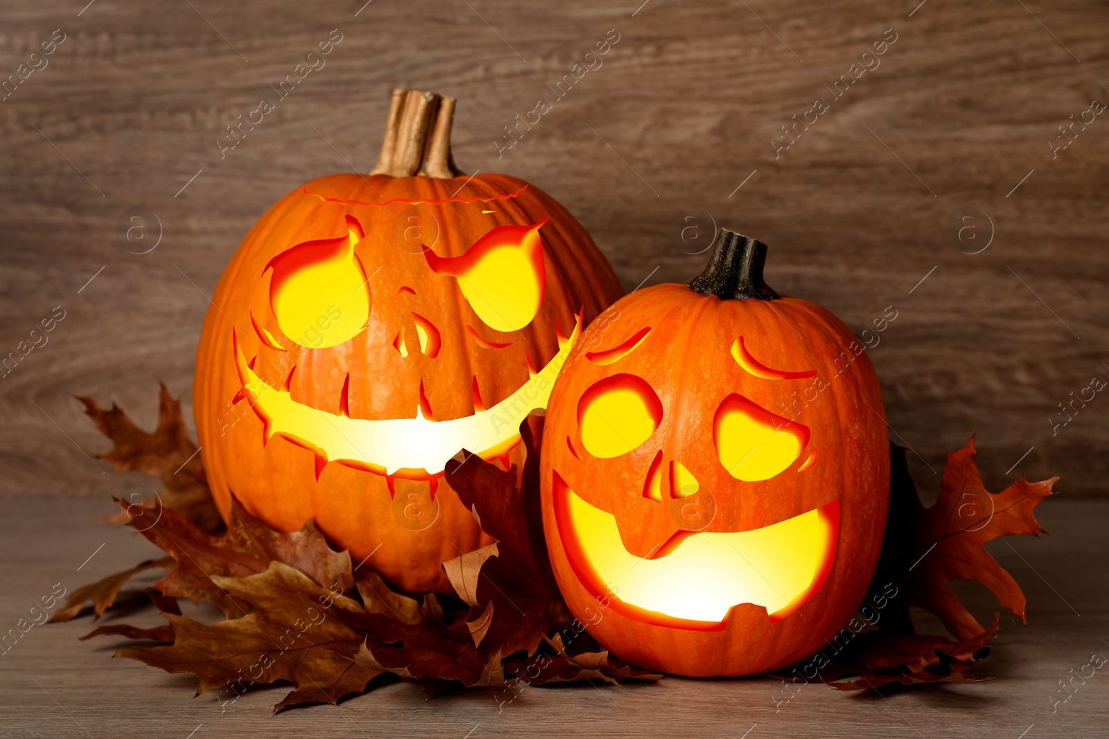 Image of Spooky jack o`lanterns and dry autumn leaves on wooden table. Halloween decor
