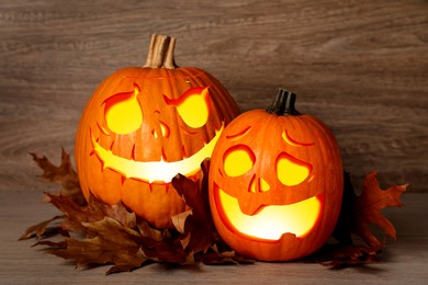 Image of Spooky jack o`lanterns and dry autumn leaves on wooden table. Halloween decor