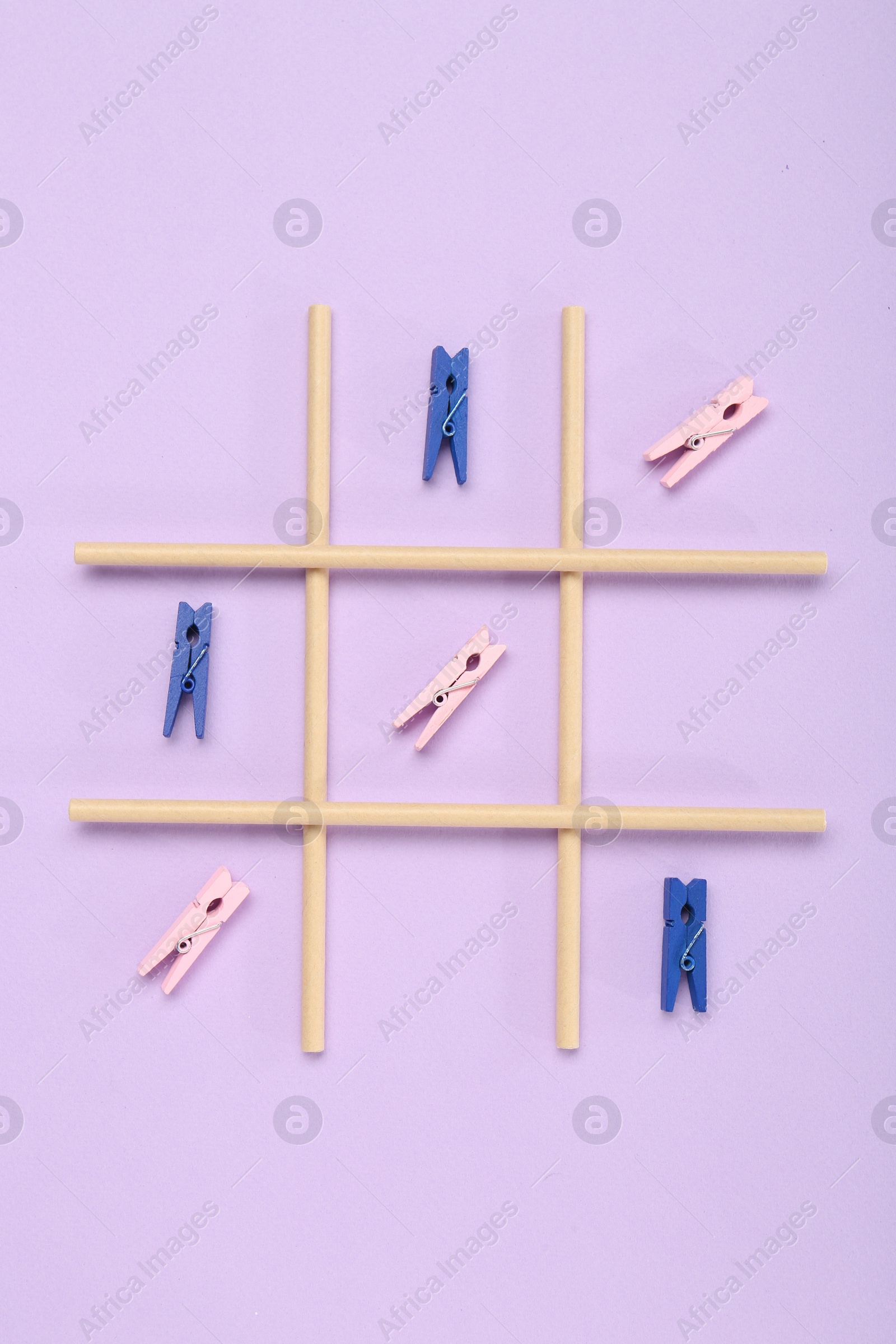 Photo of Tic tac toe game made with clothespins on lilac background, top view