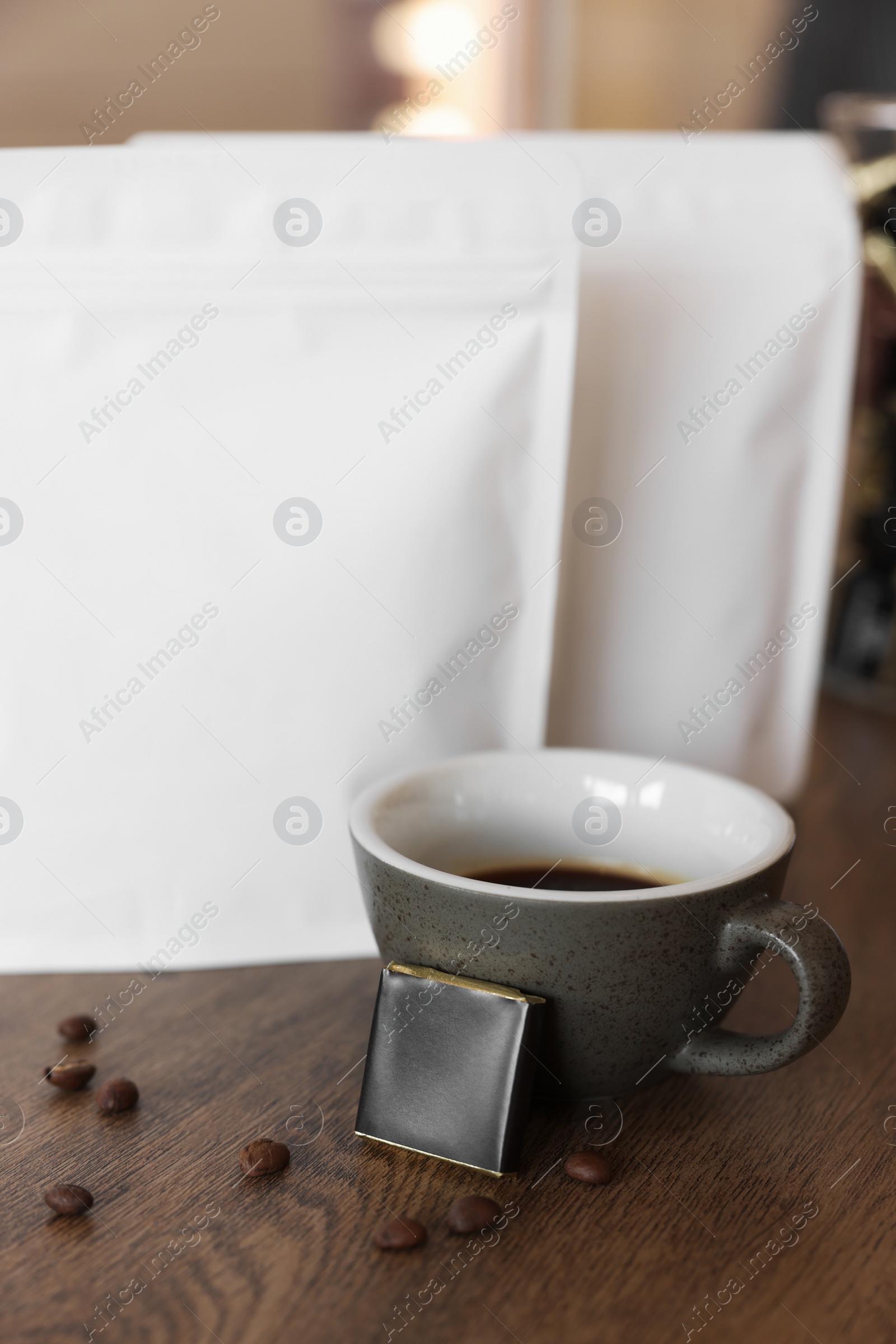 Photo of Cup of aromatic coffee, packages with beans and chocolate on wooden table indoors