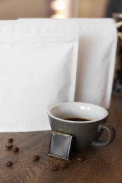 Cup of aromatic coffee, packages with beans and chocolate on wooden table indoors