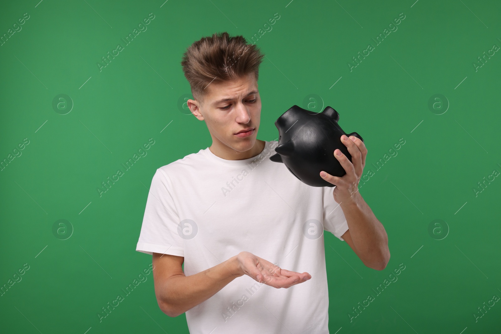 Photo of Upset man with empty piggy bank on green background