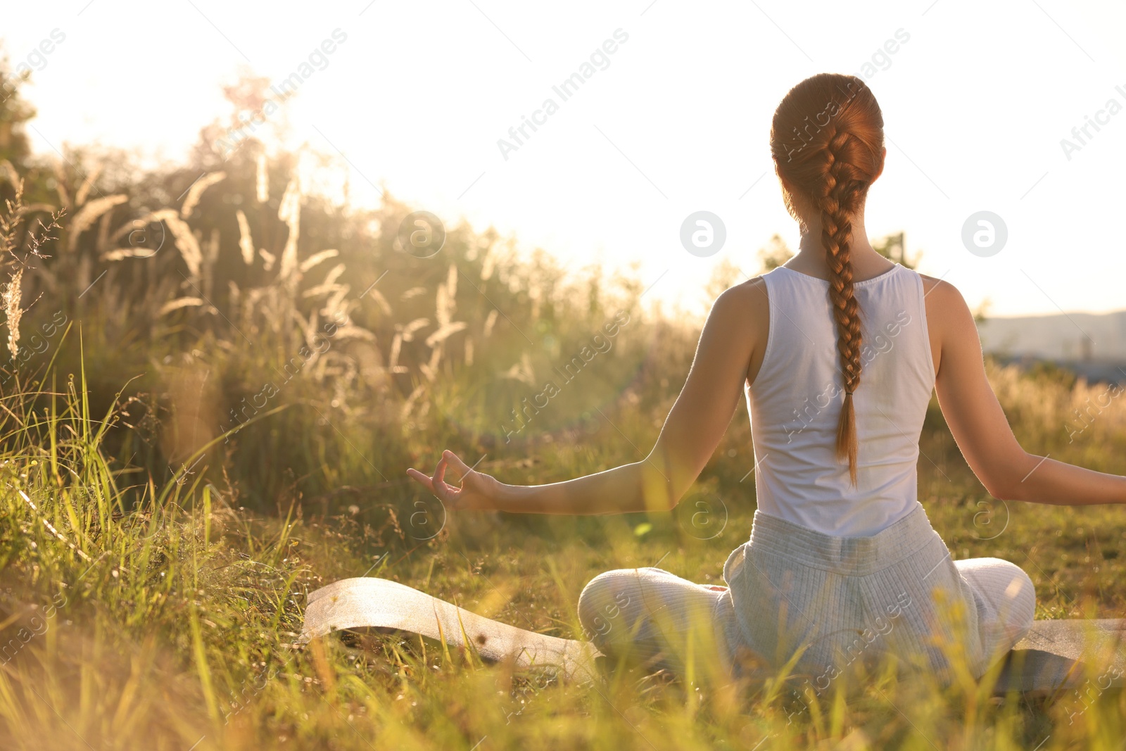 Photo of Woman practicing Padmasana on yoga mat outdoors on sunny day, back view. Lotus pose