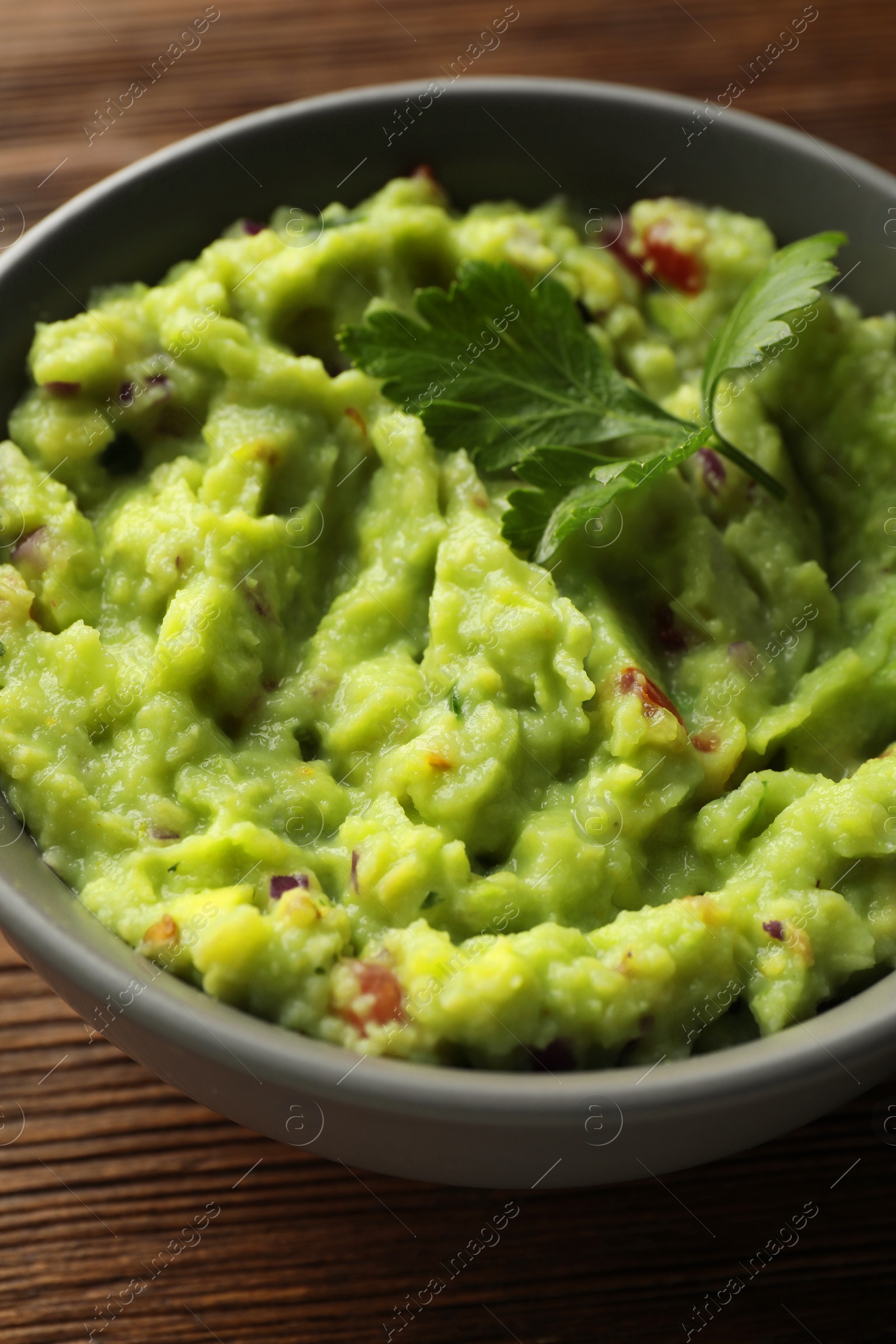 Photo of Bowl of delicious guacamole with parsley on table, closeup