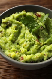 Photo of Bowl of delicious guacamole with parsley on table, closeup