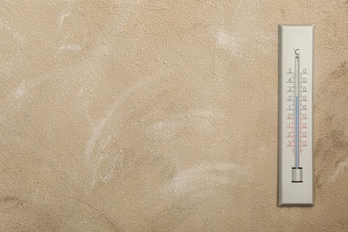 Weather thermometer on beige wall. Space for text