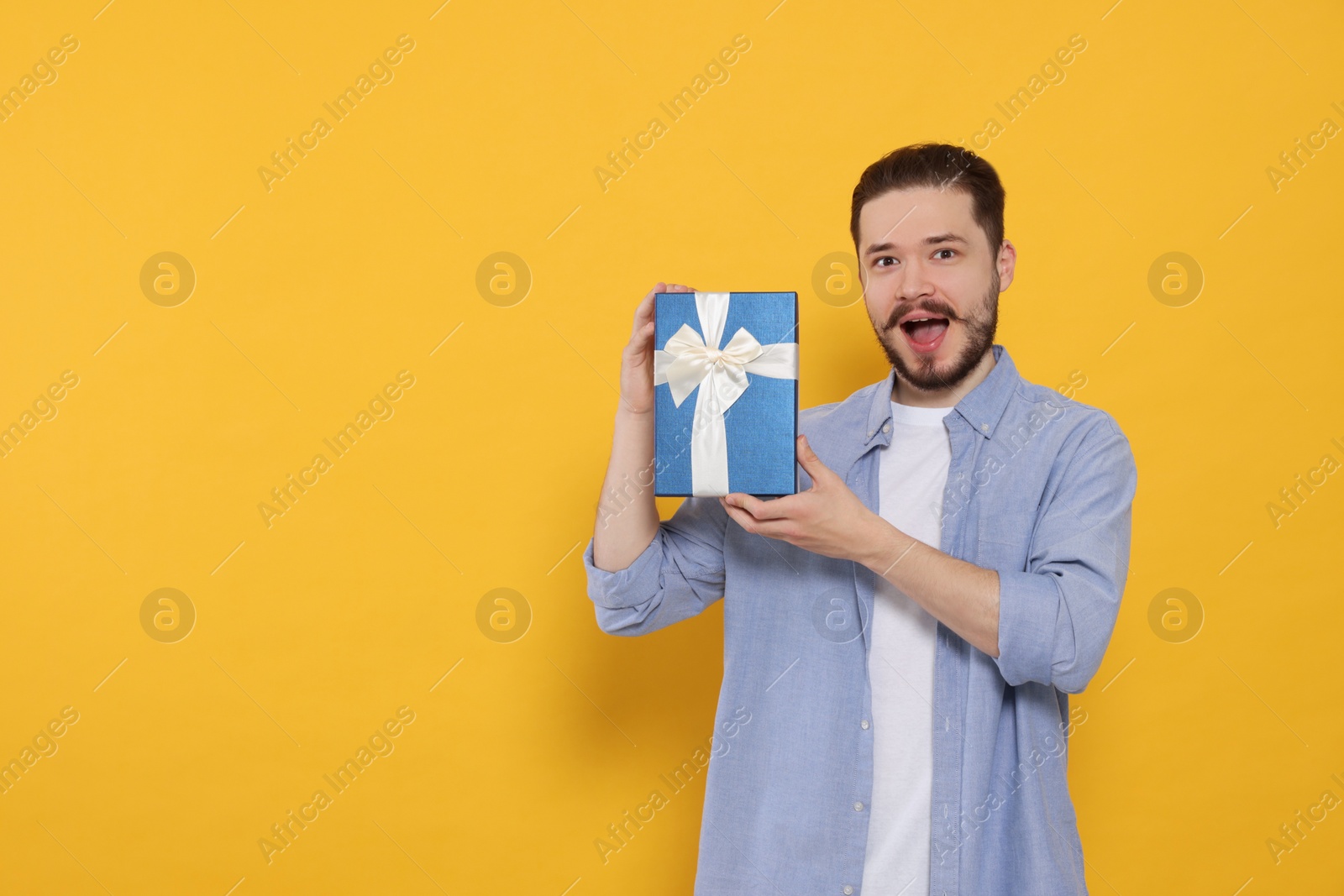 Photo of Emotional man with gift on orange background. Space for text