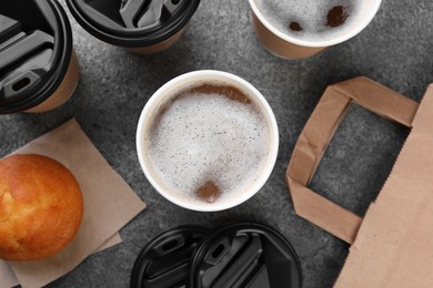 Photo of Coffee to go. Paper cups with tasty drink and muffin on grey table, flat lay