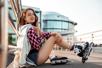 Photo of Beautiful young woman with roller skates sitting outdoors