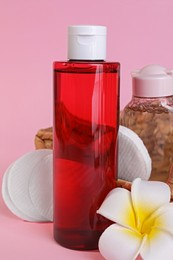 Photo of Bottles of micellar water, plumeria flower and cotton pads on pink background