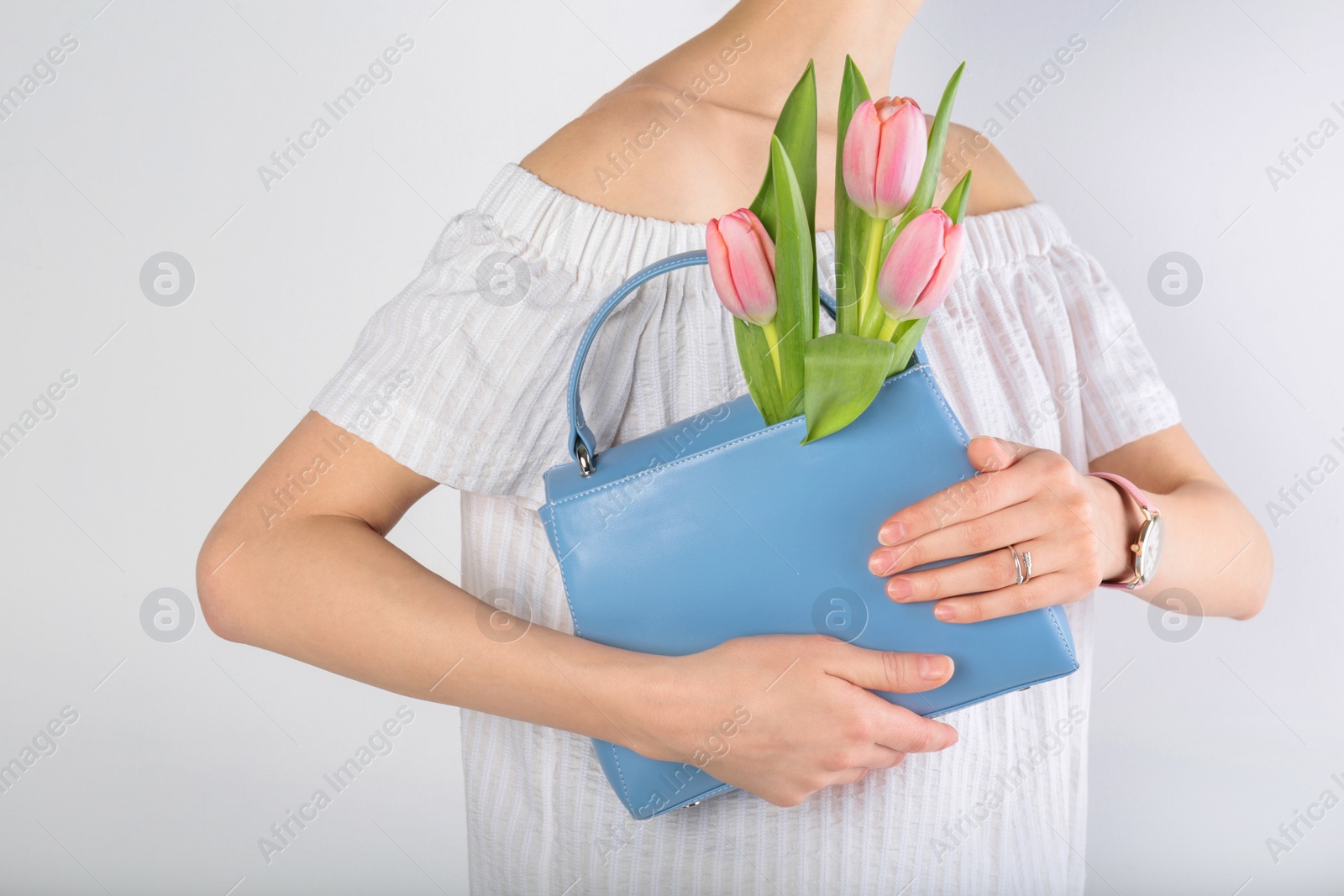 Photo of Stylish woman with handbag and spring flowers against light background, closeup