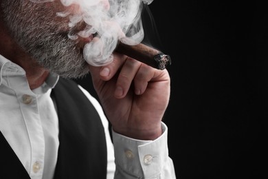 Photo of Bearded man smoking cigar against black background, closeup. Space for text
