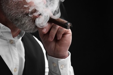 Bearded man smoking cigar against black background, closeup. Space for text