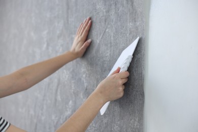 Woman smoothing stylish gray wallpaper in room, closeup