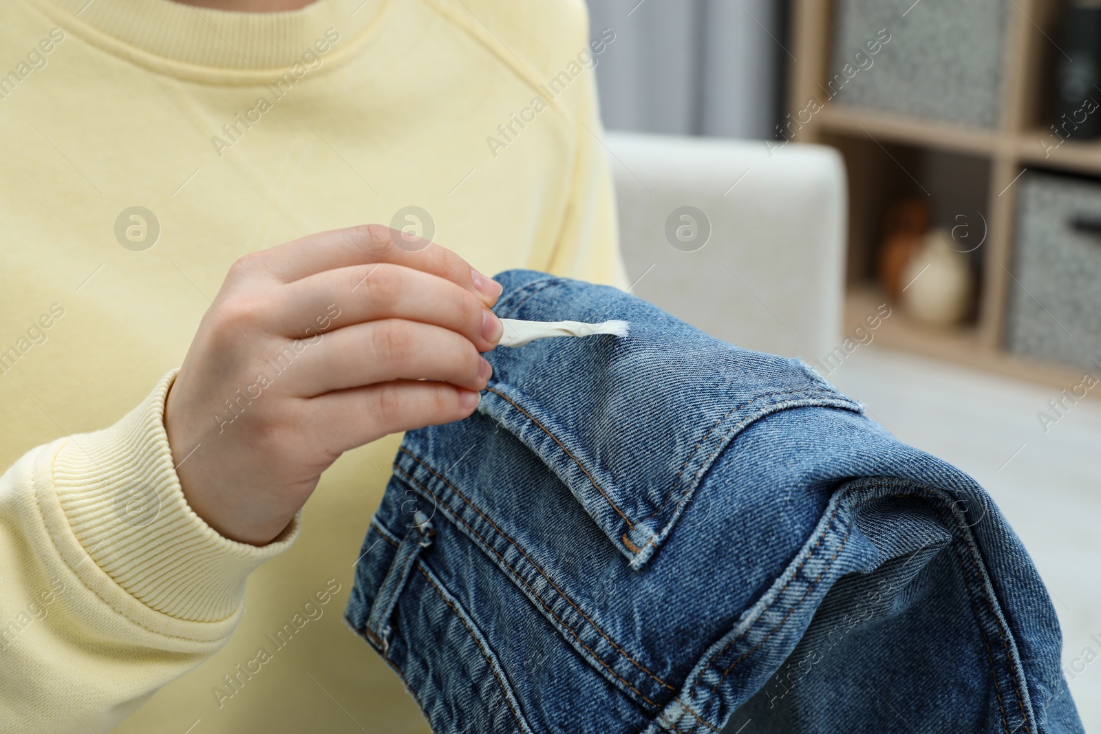 Photo of Woman removing chewing gum from jeans indoors, closeup