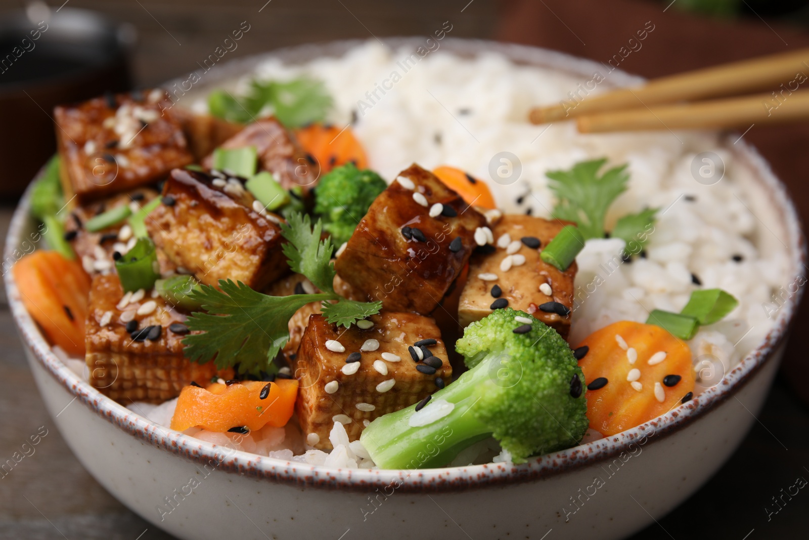 Photo of Bowl of rice with fried tofu, broccoli and carrots on table, closeup