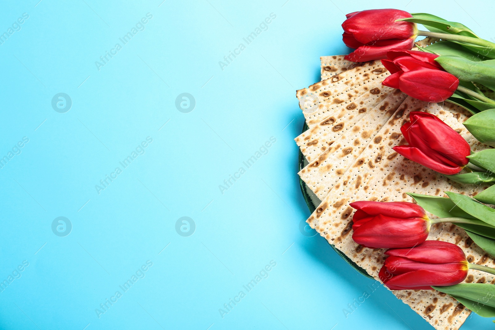 Photo of Matzos and flowers on light blue background, flat lay with space for text. Passover (Pesach) Seder