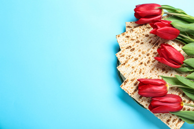 Matzos and flowers on light blue background, flat lay with space for text. Passover (Pesach) Seder