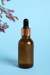 Photo of Bottle with cosmetic oil on podium and flowers on light blue background