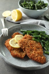 Photo of Tasty schnitzels served with lemon and green beans on grey table, closeup