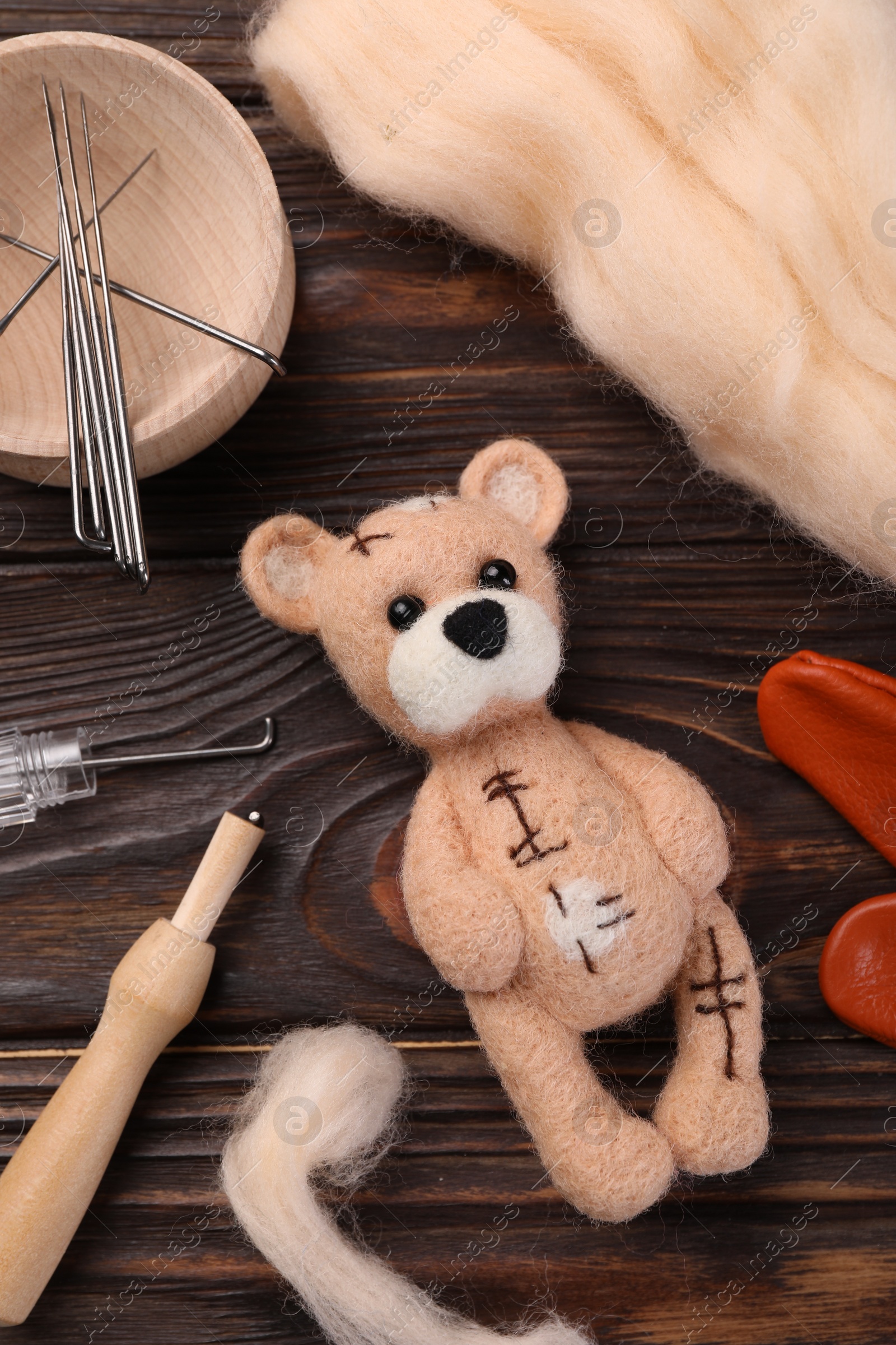 Photo of Felted bear, wool and tools on wooden table, flat lay