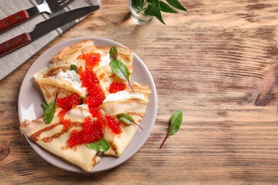 Thin pancakes with red caviar on plate, top view