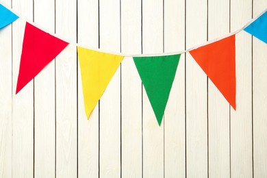 Photo of Bunting with colorful triangular flags on white wooden background. Festive decor