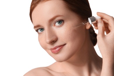 Photo of Beautiful woman with freckles applying cosmetic serum onto her face on white background